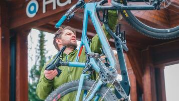 A person holding a mountain bike in front of a wooden structure with a sign that reads "Ava".