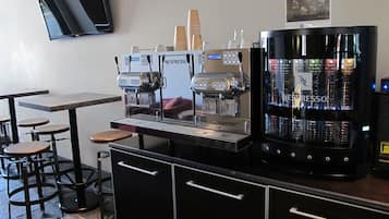 Un café-bar équipé de deux machines à expresso, d’un moulin à café et d’un réfrigérateur rempli de produits Nespresso. On y trouve également des tabourets et un téléviseur à écran plat fixé au mur.