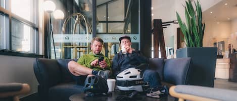 Two people sitting on a couch in a modern lobby with large windows and a potted plant.