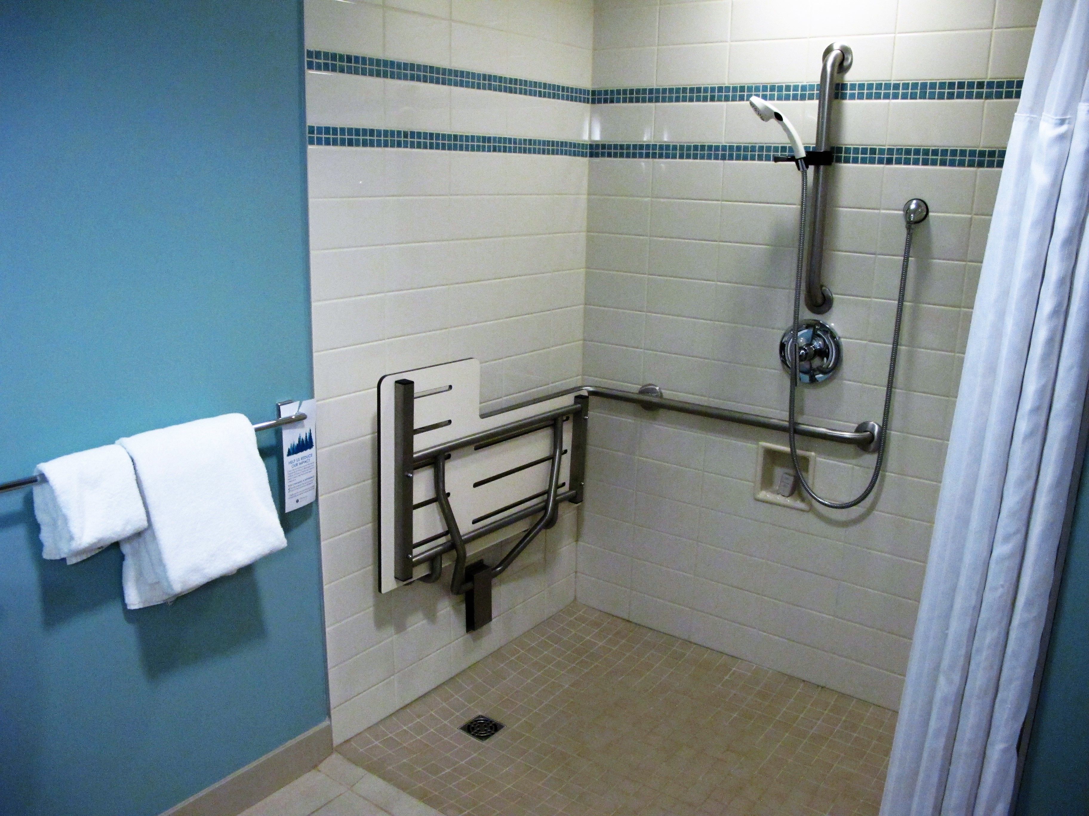 A bathroom with a shower, grab bars, a towel rack, and a tiled floor.