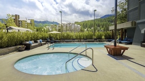 Un espace piscine avec des chaises longues, une table en bois et une vue sur les montagnes.