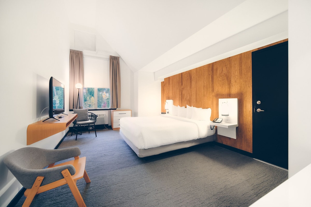 Habitación de hotel con cama, escritorio, silla y un armario grande.