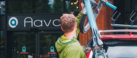 A person carrying a bicycle over a red car in front of a building with a sign that reads "Ava".