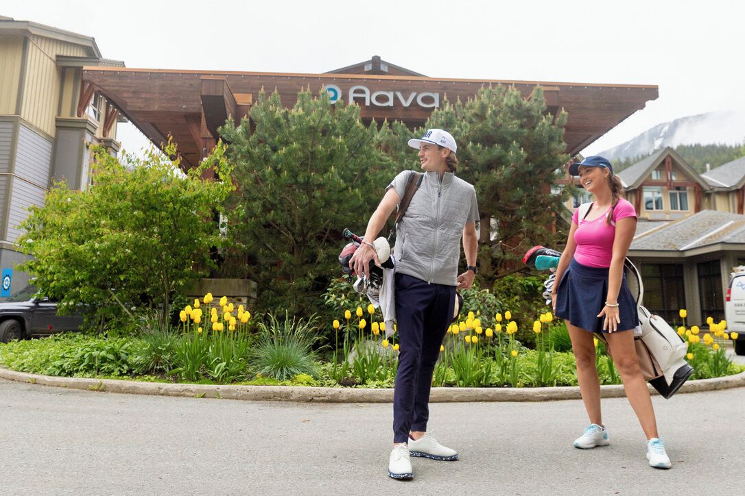 Two people walking in front of a building with a sign that reads "Aava".