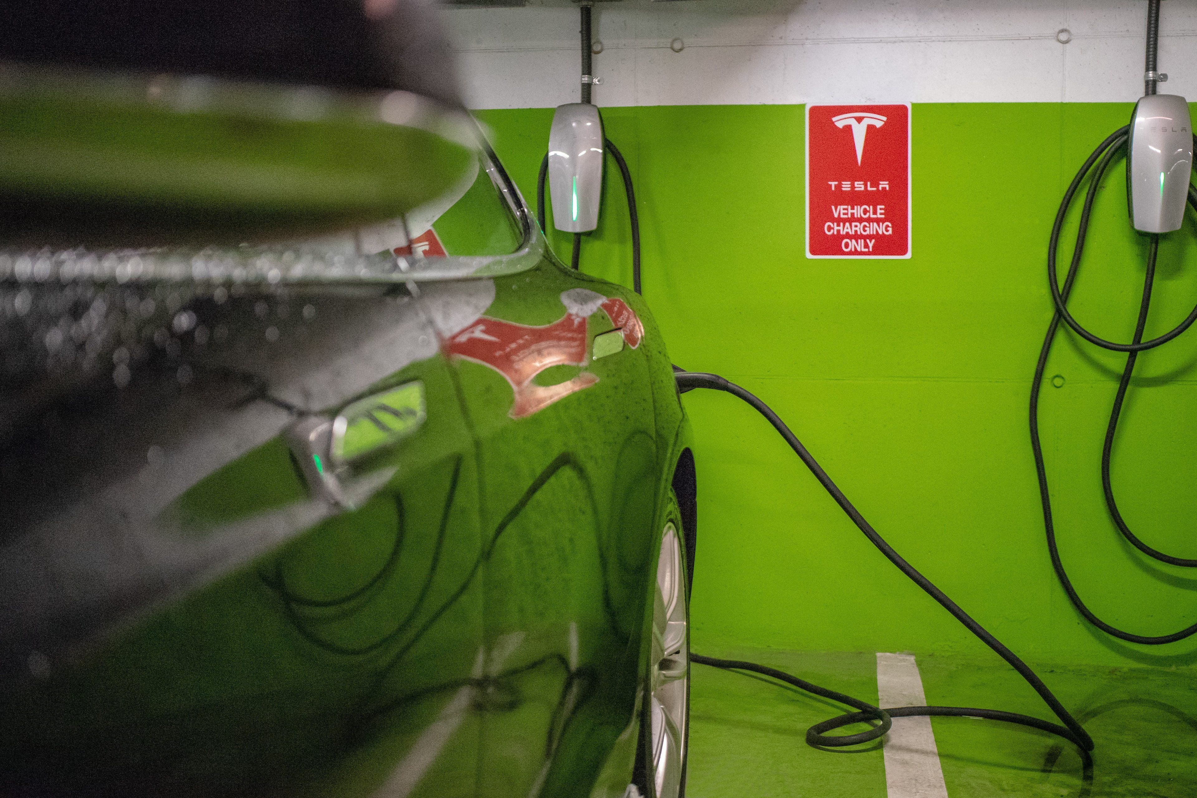 A Tesla charging station in a parking garage with a green wall and a sign indicating it is for Tesla vehicles only.