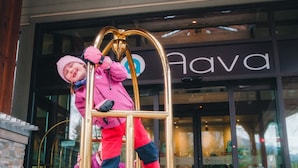 Un enfant, vêtu d’une tenue rose, grimpe sur un chariot doré devant un bâtiment sur lequel est apposée une enseigne indiquant « Hava ».