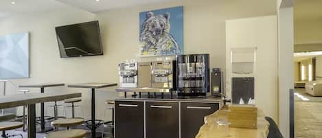 A modern bar area with espresso machines, seating, and a large bear painting on the wall.