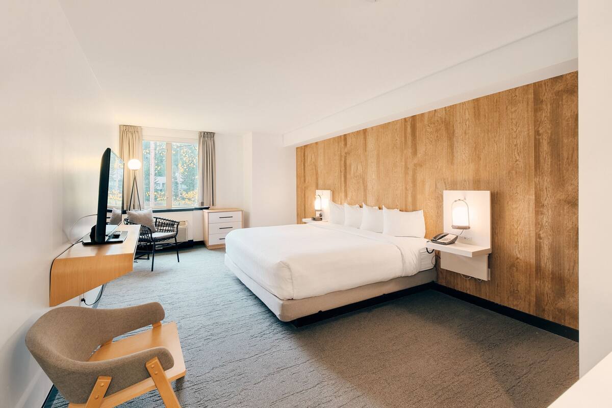 Habitación de hotel moderna con una cama grande, lámparas de noche, un escritorio con computadora y una silla.