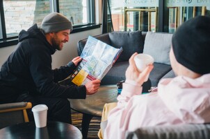 Una persona leyendo un mapa en un ambiente interior acogedor, con un sofá y una mesa.