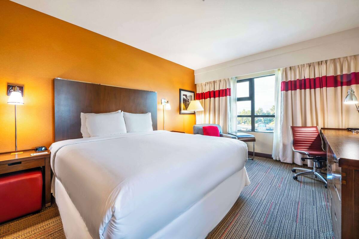 A hotel room with a large bed, a desk, a chair, and a window with curtains.