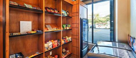 A pantry with shelves stocked with snacks and beverages, a Nestlé freezer, and a view of the outside through large windows.