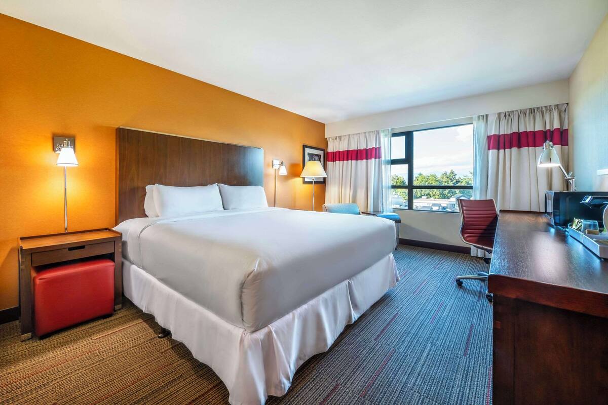A hotel room with a large bed, a desk, a chair, and a window with curtains.