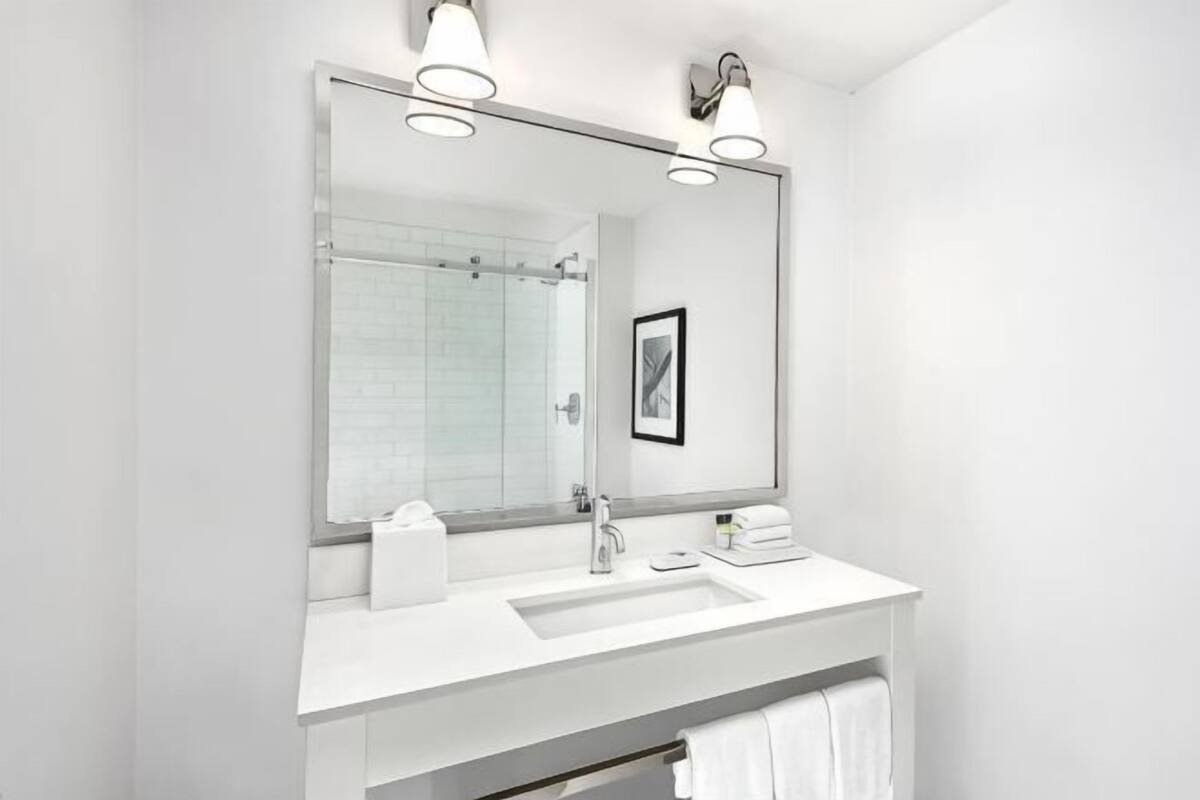 A modern bathroom with a large mirror, white sink, and towel rack.