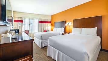 A hotel room with two beds, a desk, a TV, and a window with curtains.