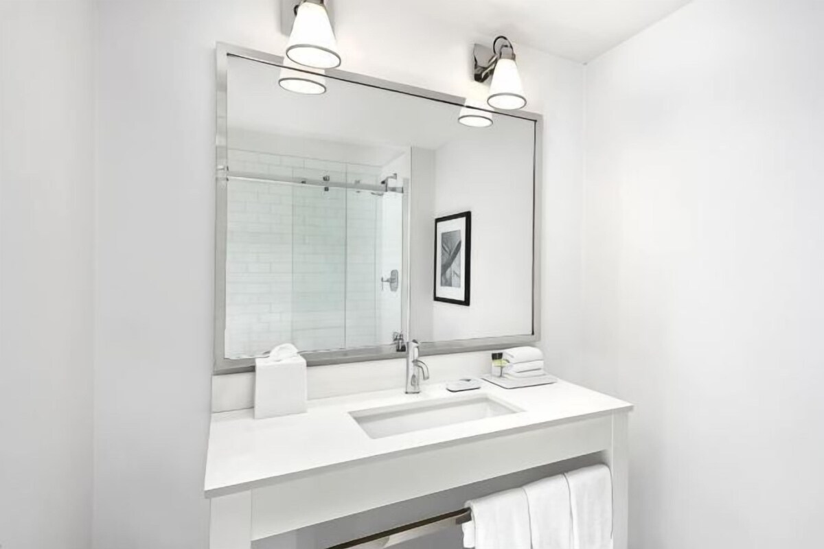 A modern bathroom with a large mirror, white sink, and towel rack.