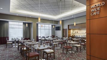 Een ruim café in een hotel met meerdere tafels en stoelen, grote ramen en een modern plafondontwerp.