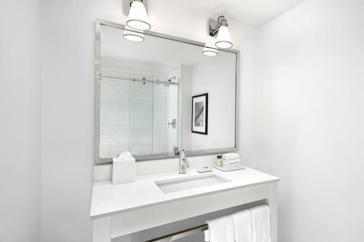 A modern bathroom with a large mirror, white sink, and towel rack.