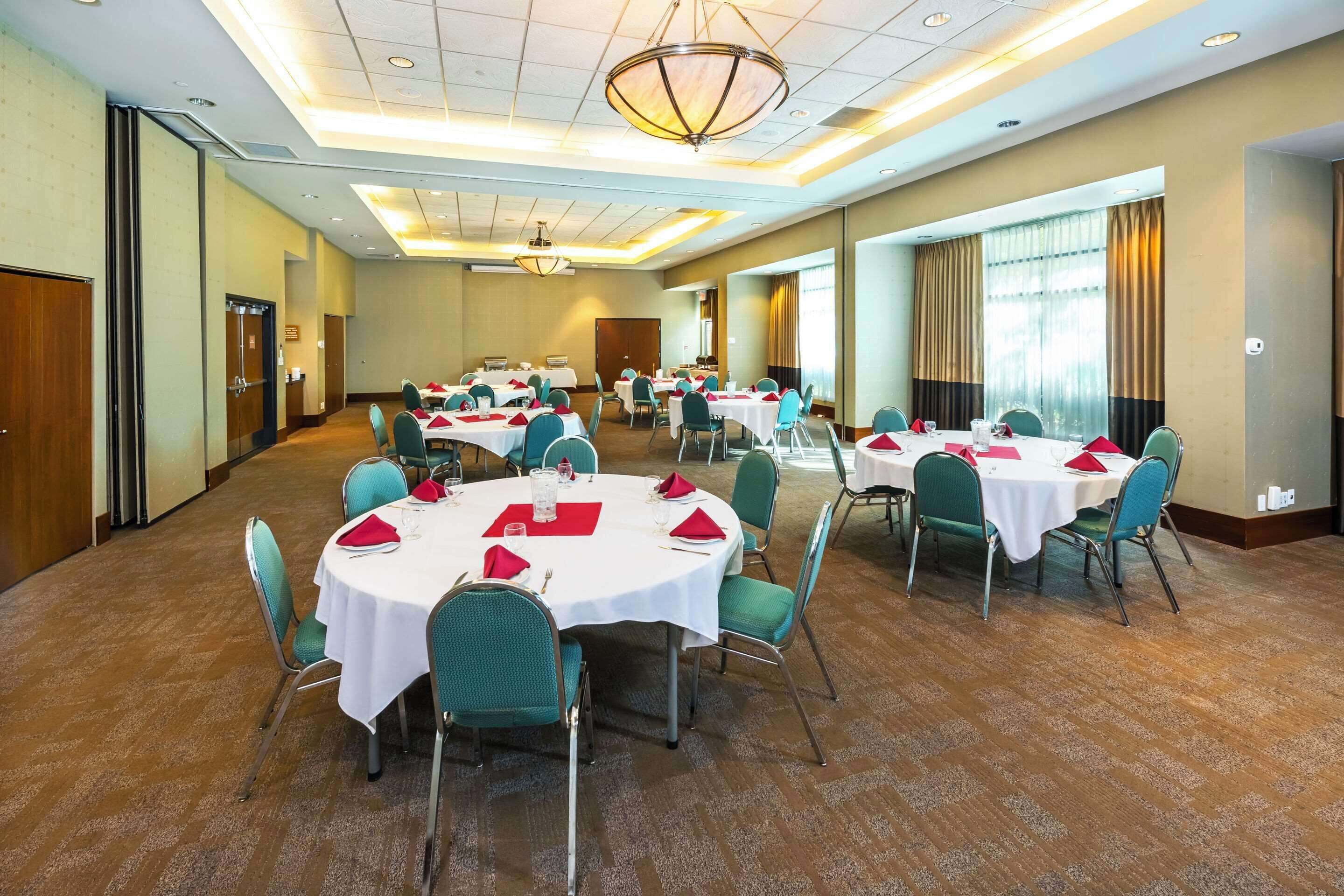 Un salón de conferencias con varias mesas redondas, cada una cubierta con manteles blancos, servilletas rojas y sillas color turquesa.