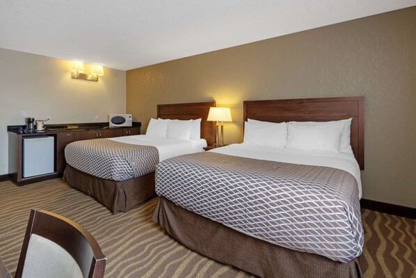 A hotel room with two beds, a desk with a lamp, a microwave, and a small refrigerator.
