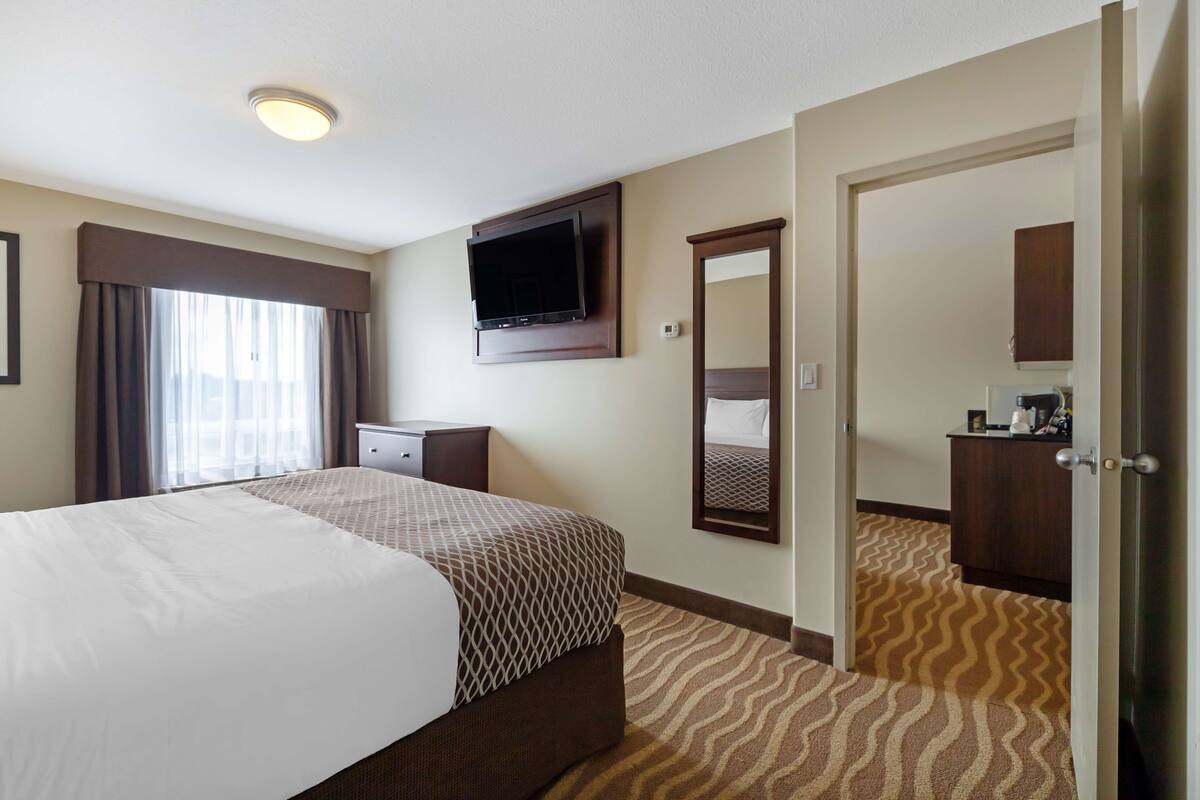 Una habitación de hotel con una cama, un televisor montado en la pared, un aparador y un espejo.