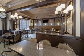 A restaurant interior with a bar area, dining tables, chairs, a clock, and wall-mounted light fixtures.