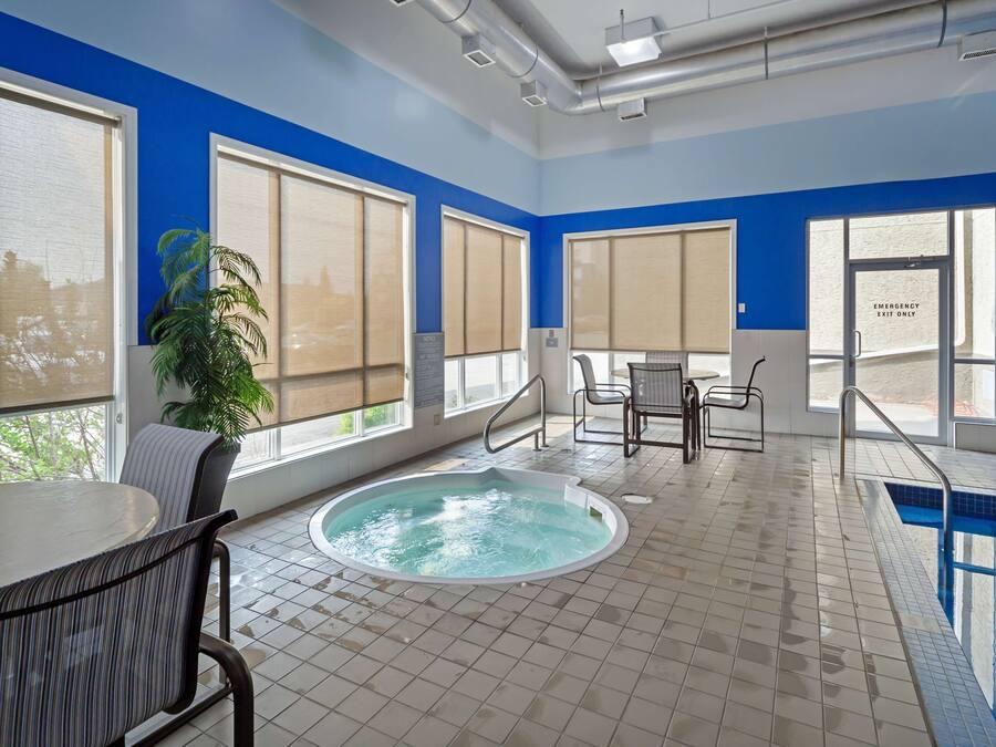 A modern indoor pool area with a hot tub, large windows, and a seating area.