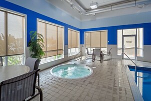 Un espace piscine intérieur moderne, doté d’un jacuzzi, de grandes fenêtres et d’un coin salon.