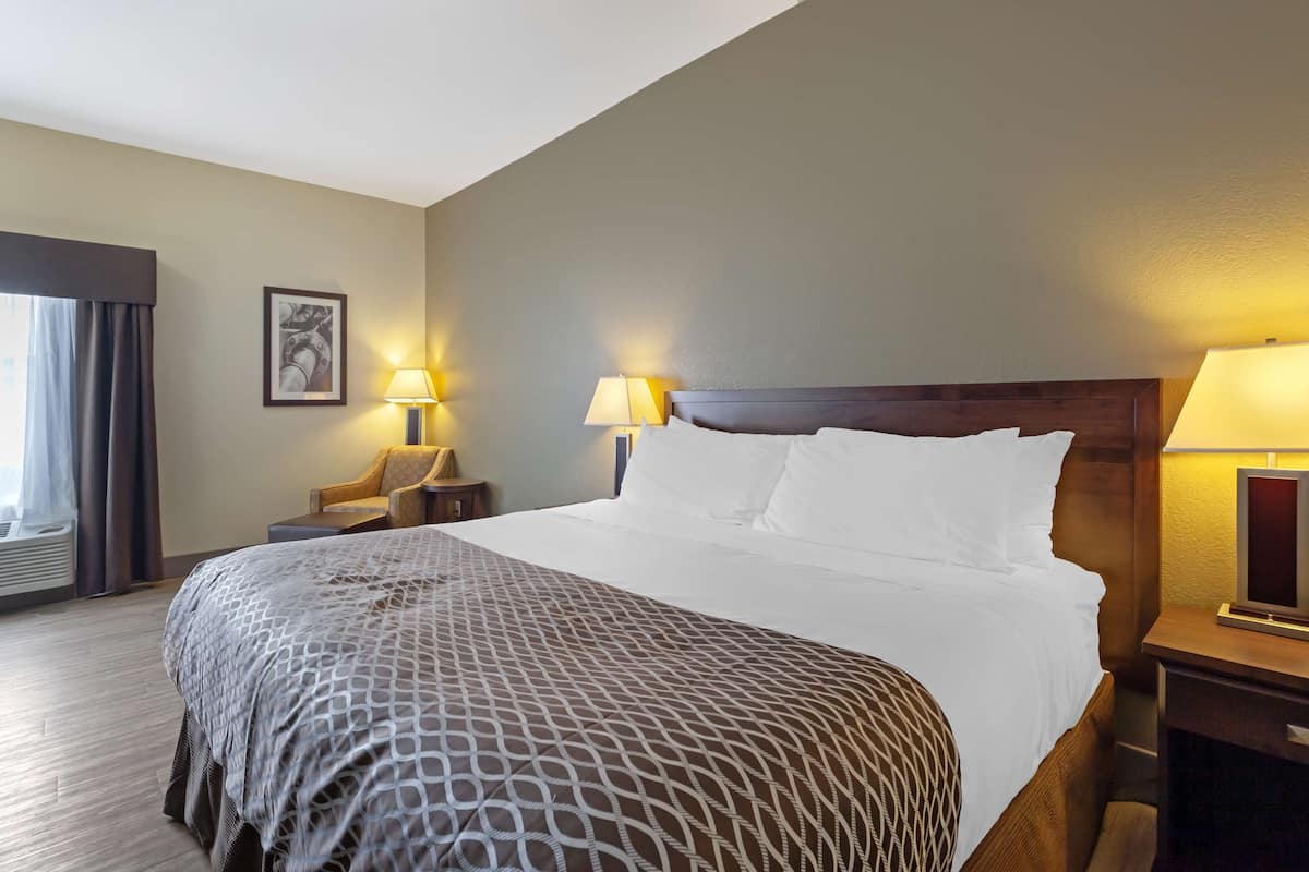 Habitación de hotel con una cama grande, dos lámparas de noche, una silla, una mesita y un cuadro en la pared.