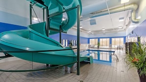 A teal spiral slide in a room with a pool, tiled floor, and blue walls.