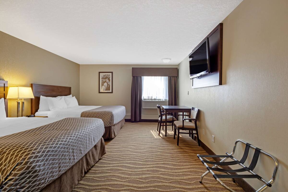 Habitación de hotel con dos camas, un escritorio, una silla, un televisor montado en la pared y una ventana con cortinas.