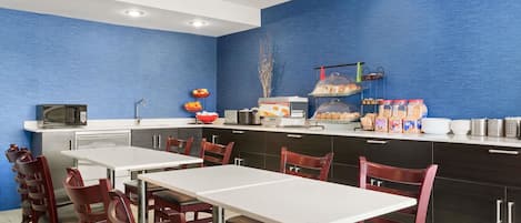 A modern kitchen with blue walls, stainless steel appliances, and a breakfast bar with various food items.