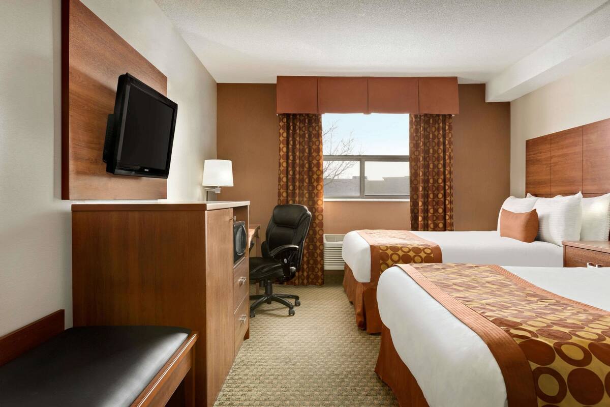 A hotel room with two beds, a desk, a chair, a television, and a window with curtains.