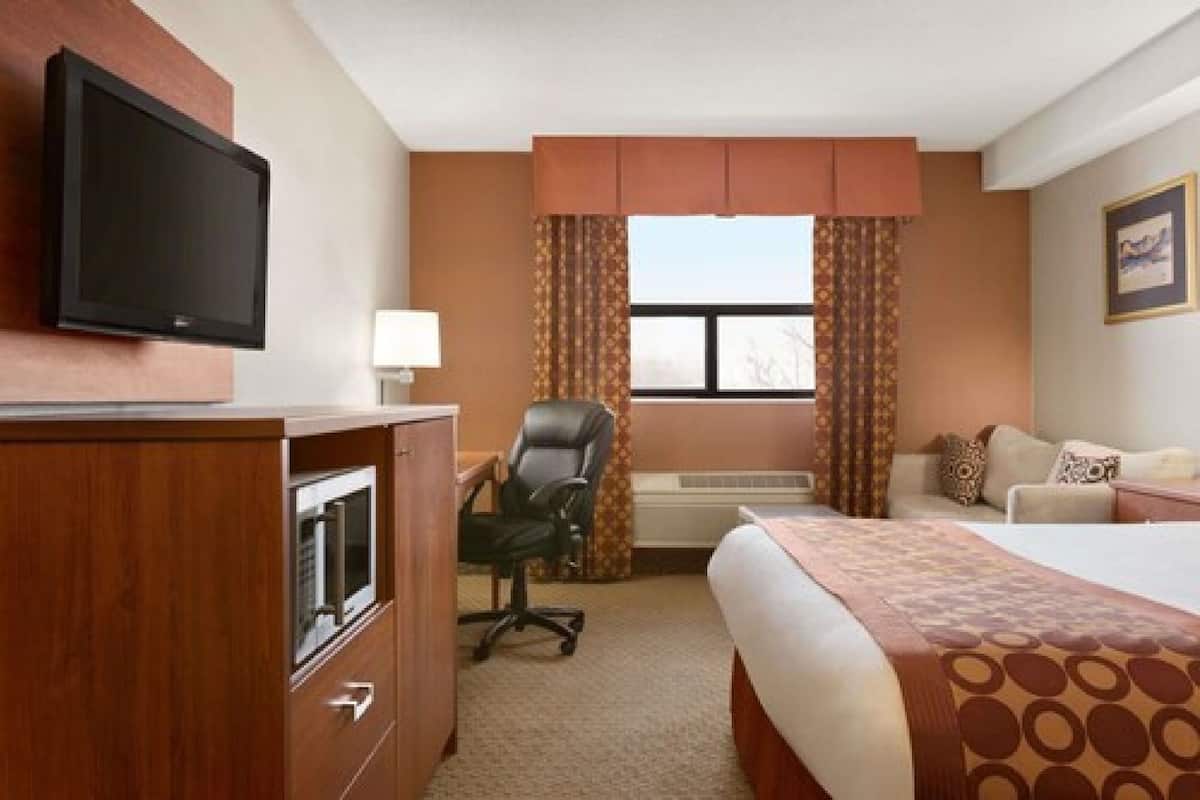 A hotel room with a bed, a desk with a chair, a television, and an air conditioning unit.