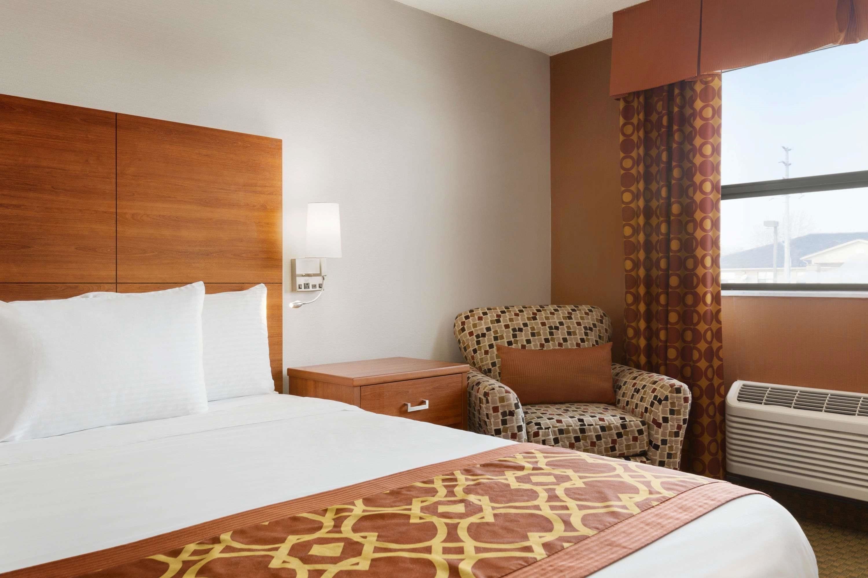 A hotel room with a large bed, a patterned armchair, a bedside table, and a window with curtains.