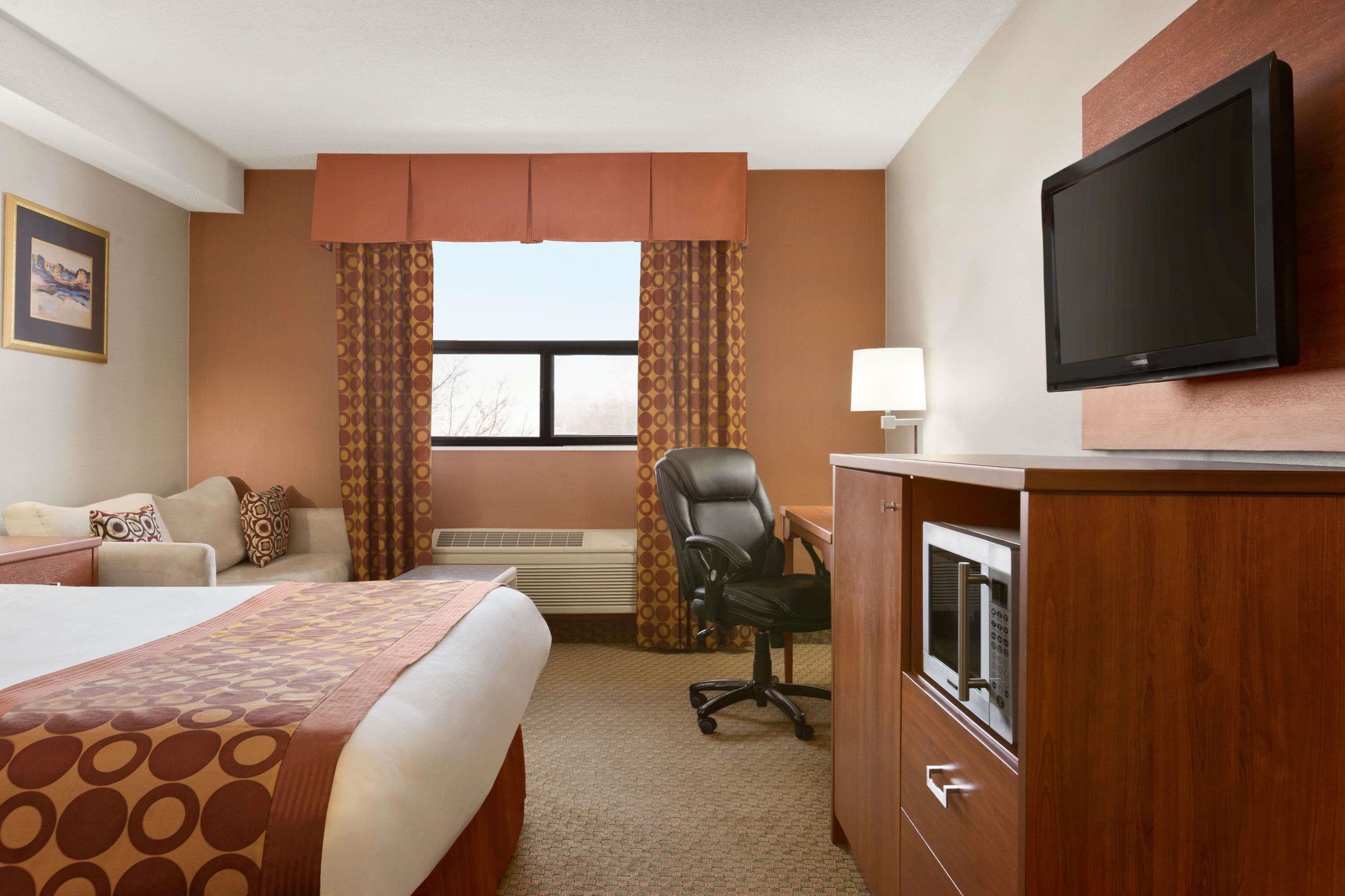 A hotel room with a bed, a desk, a chair, a television, and a window with curtains.