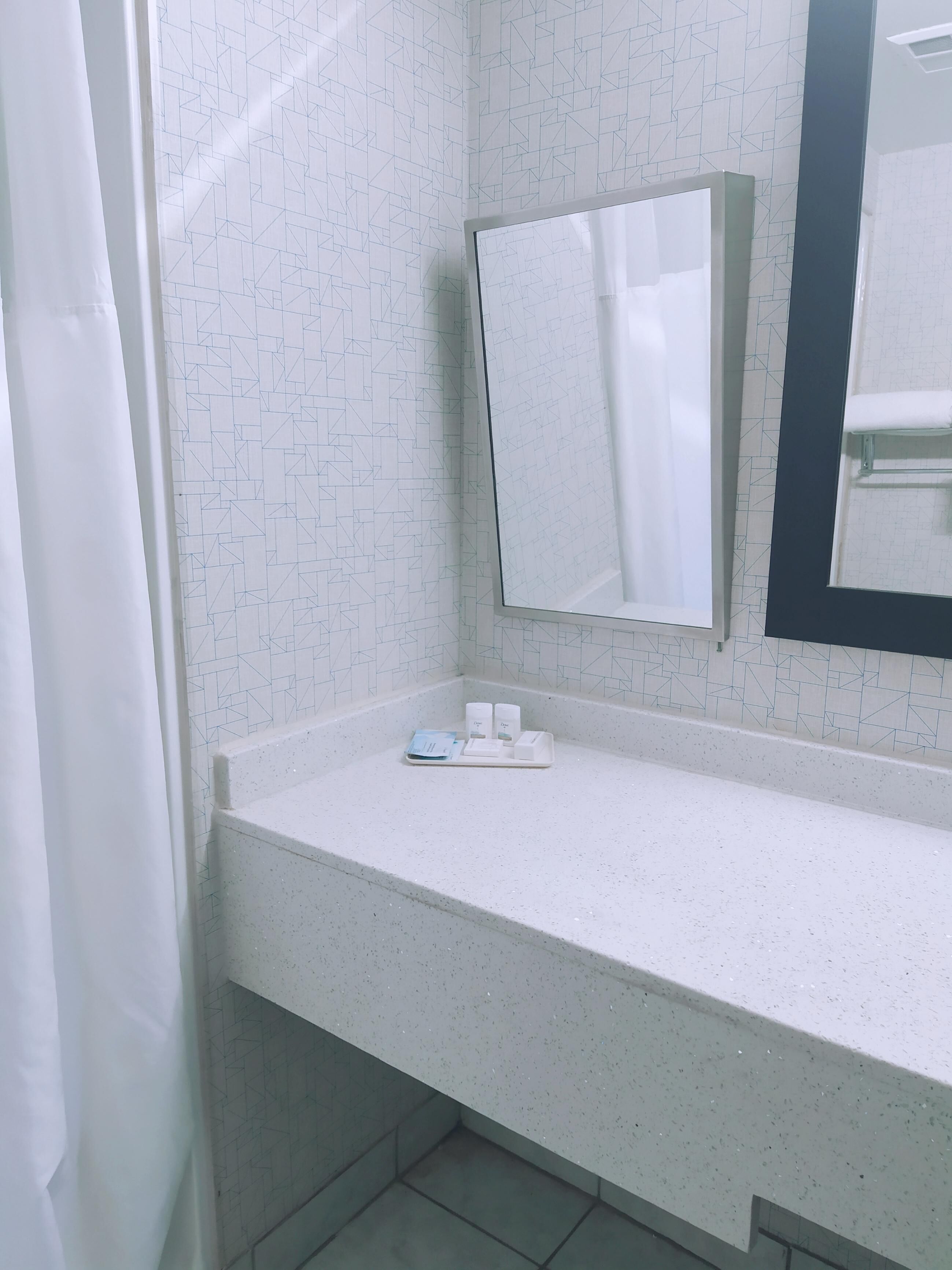 A bathroom with a white tiled wall, a white countertop, a mirror, and a shower curtain.