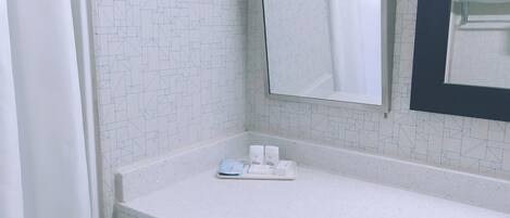 A bathroom with a white tiled wall, a white countertop, a mirror, and a shower curtain.