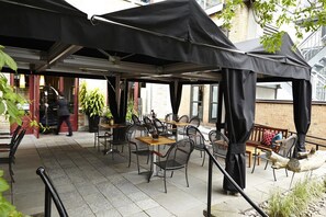 An outdoor cafe with tables and chairs, covered by black canopies, and a person walking by. - Hôtel Le Germain Québec (Québec City)