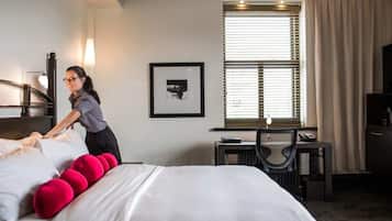 A hotel room with a neatly made bed, a desk with a chair, a framed picture on the wall, and a window with blinds.
