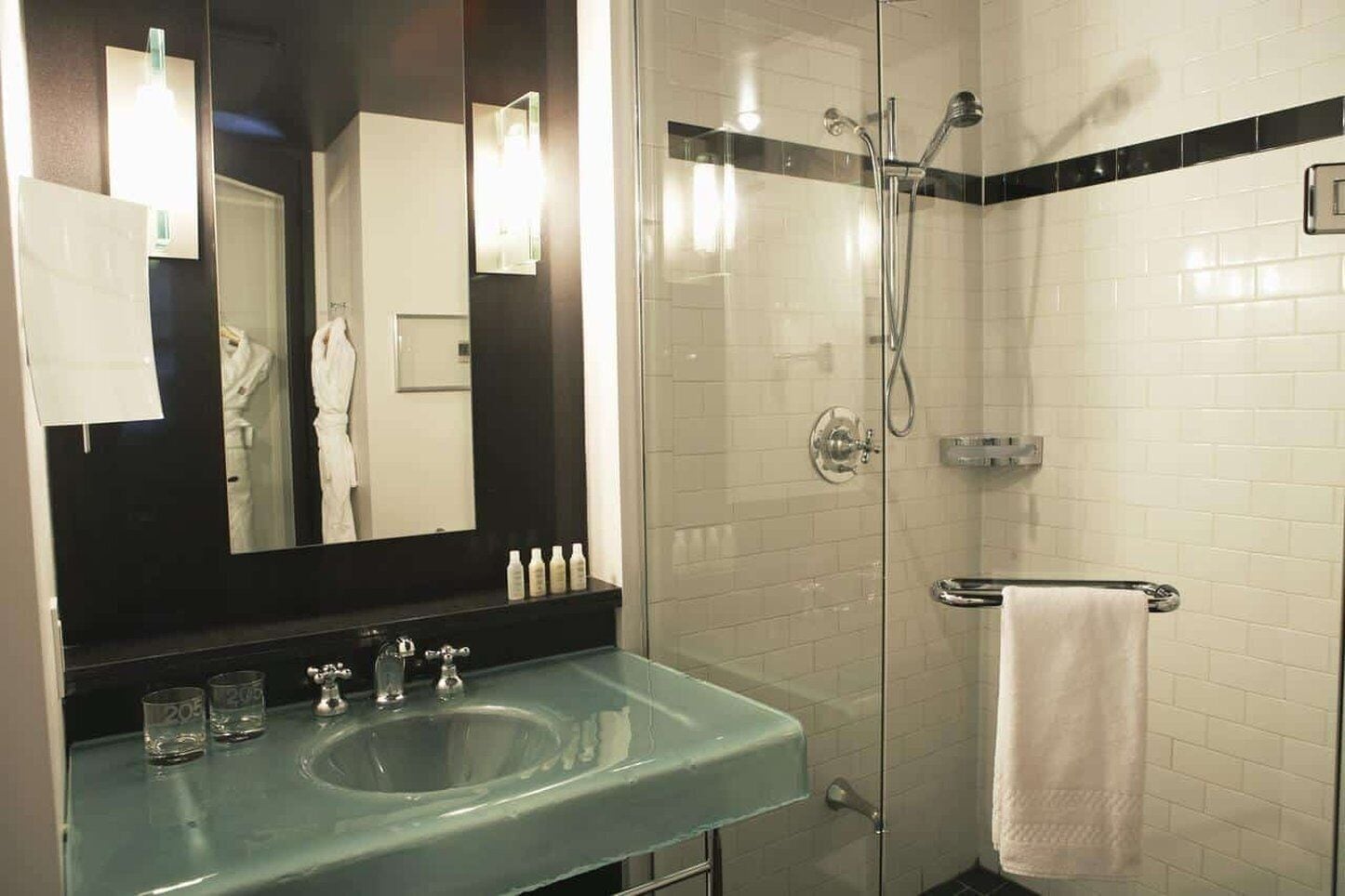 Un baño moderno con un lavabo de vidrio, un espejo grande, una ducha con cerramiento de vidrio y un perchero para toallas.