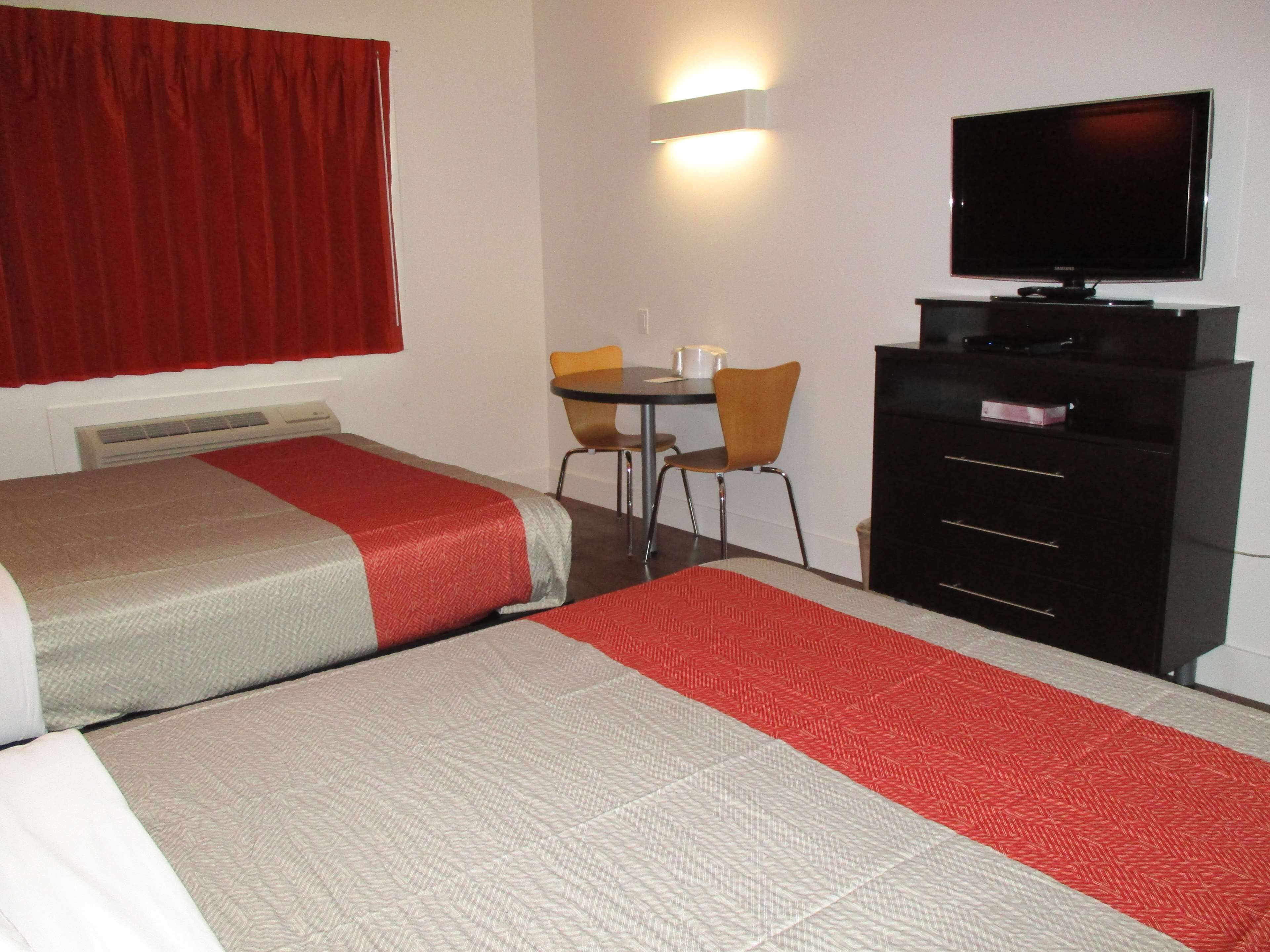 A hotel room with two beds, a desk with a chair, a television, and a dresser.
