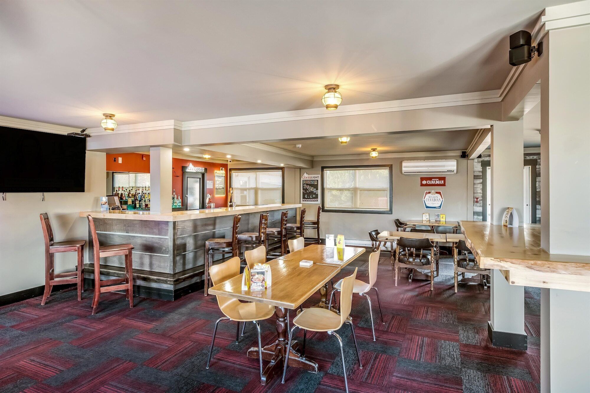 Un restaurant doté d’un bar, de tables et de chaises en bois, et d’un sol recouvert d’une moquette rouge.