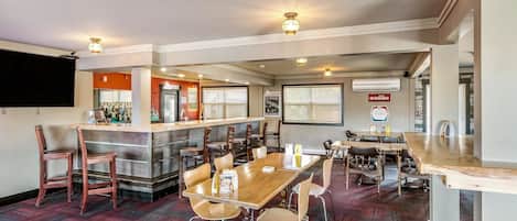 Un restaurante con zona de bar, mesas y sillas de madera, y suelo cubierto de alfombra roja.