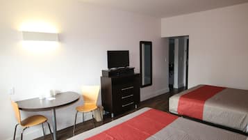 A hotel room with a bed, a desk with a chair, a television, a dresser, and a mirror.