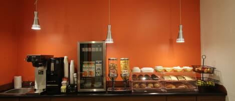 A breakfast bar with coffee machines, a refrigerator, and various food items.