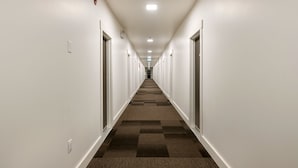 Un pasillo de hotel con paredes blancas, piso alfombrado y puertas a ambos lados.