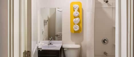 Baño con inodoro, lavamanos y ducha. Hay un toallero amarillo con tres toallas.