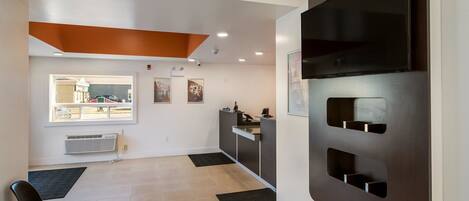 A modern hotel lobby with a reception desk, a black chair, a large window, and a wall-mounted TV.