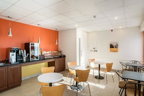 Un café moderno con una máquina de café, una zona de estar y una pared de acento naranja brillante.