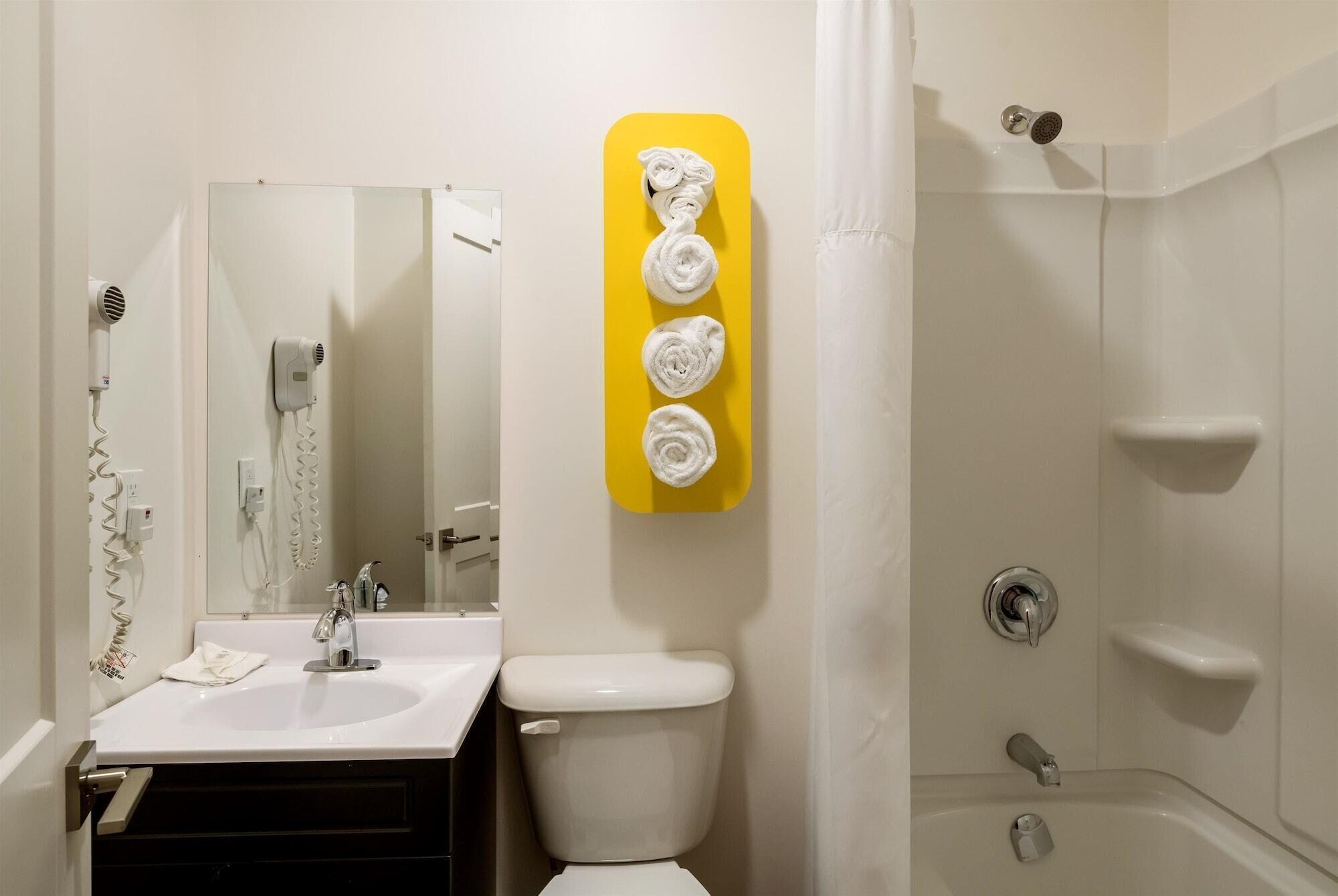 Un bany amb un lavabo, vàter i plat de dutxa. Hi ha un penjador groc amb tres tovalloles.